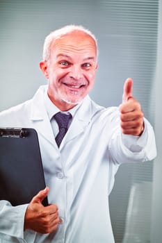 Mature, male doctor is smiling and giving a thumbs up gesture while holding a clipboard, expressing confidence and positive outcome in healthcare