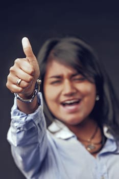 Enthusiastic young indian woman smiling and giving a thumbs up, radiating positivity and approval against a dark background, embodying confidence and motivation