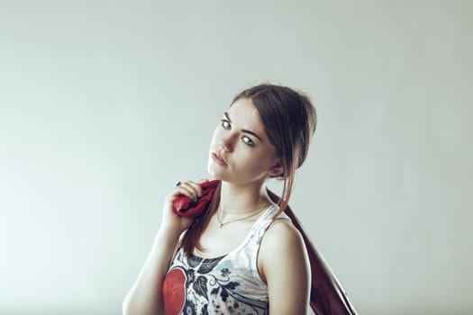 Portrait of a fashionable young woman holding a red leather jacket over her shoulder, looking confidently at the camera against a light gray background