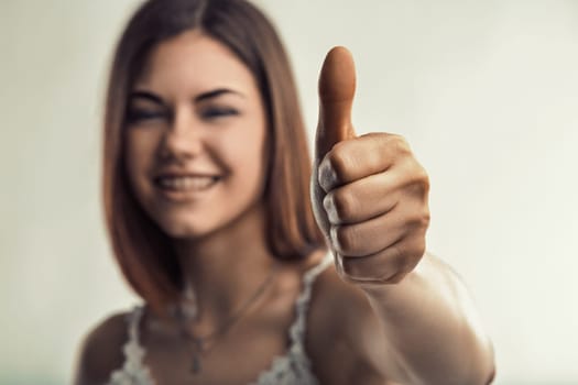 Young woman smiling and giving a thumbs up, radiating positivity and confidence while expressing her satisfaction and agreement through an encouraging gesture of approval