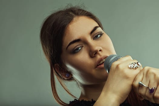 Young woman singer with an intense gaze, holding a microphone and passionately performing in a music studio, radiating her love for music and artistic expression
