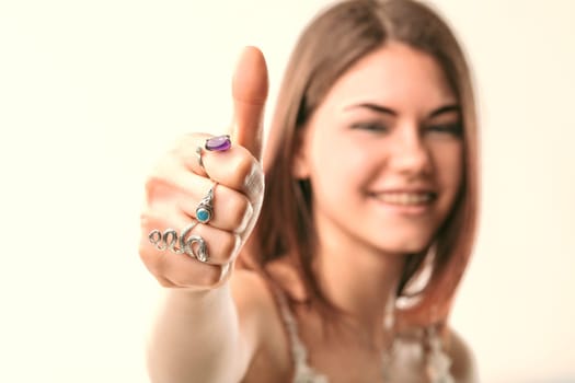 Smiling young woman giving a thumbs up while wearing stylish silver rings adorned with colorful gemstones, radiating positivity and approval against a clean white background