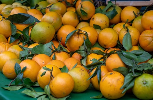 A pile of oranges with green leaves. The oranges are ripe and ready to be eaten