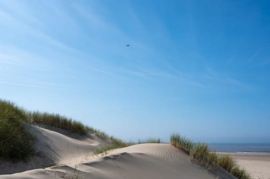 View over the dunes with beach grass towards the sea, on the North Sea coast in the Netherlands with a blue sky
