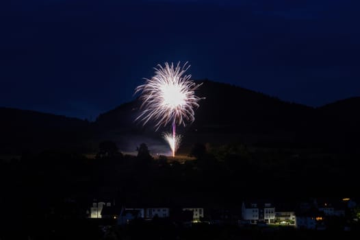 A firework rocket in the sky on a mountain at night, a few illuminated houses in the foreground,A firework rocket in the sky on a mountain at night, a few illuminated houses in the foreground