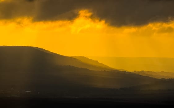 Dawn in the mountains of Crimea. A light haze of mist over the mountains and rays of the sun through the clouds.