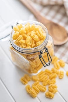 Uncooked italian pasta. Radiatori pasta in jar on a white table.