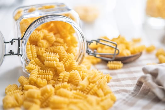 Uncooked italian pasta. Radiatori pasta in jar on a white table.