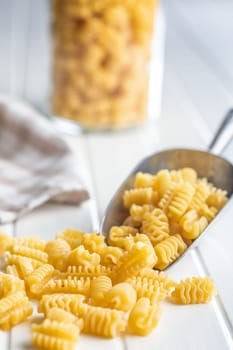 Uncooked italian pasta. Radiatori pasta in scoop on a white table.