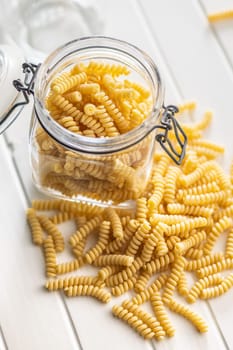 Uncooked italian pasta. Fusilli pasta in jar on a white table.