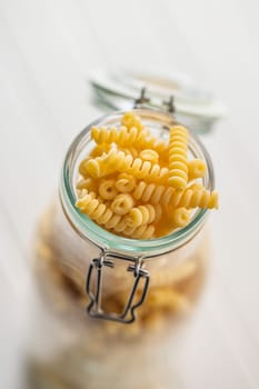 Uncooked italian pasta. Fusilli pasta in jar on a white table.