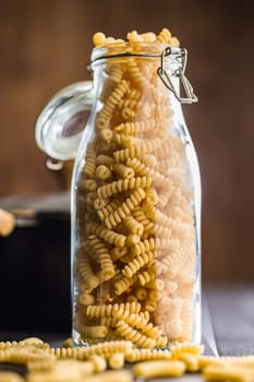 Uncooked italian pasta. Fusilli pasta in glass bottle on a black table.