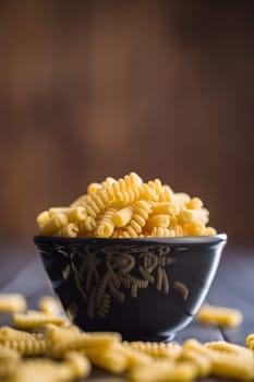 Uncooked italian pasta. Fusilli pasta in bowl on a black table.