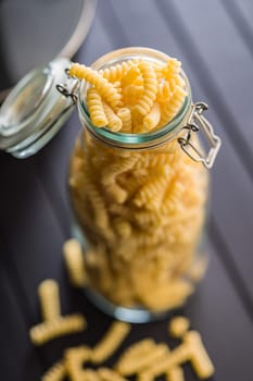 Uncooked italian pasta. Fusilli pasta in glass bottle on a black table.