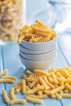 Uncooked italian pasta. Fusilli pasta in bowl on a blue table.