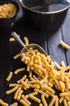 Uncooked italian pasta. Fusilli pasta in scoop on a black table.