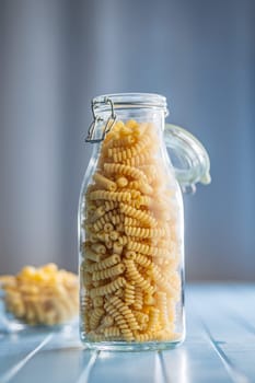 Uncooked italian pasta. Fusilli pasta in jar on a blue table.