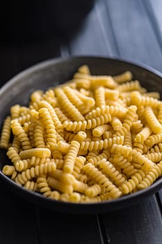 Uncooked italian pasta. Fusilli pasta in bowl on a black table.