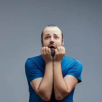 Overwhelmed by anxiety and despair, a mid-adult man biting his nails expresses deep worry while searching for solace amidst the uncertainty and emotional turmoil he faces