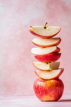 Bright red and white apple slices are neatly stacked over a whole apple, creating an artistic display on a soft pink backdrop.