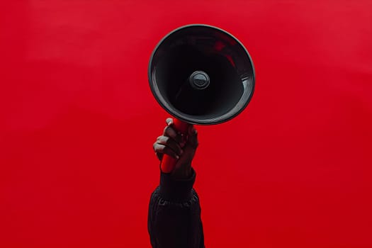 A hand holds a megaphone high against a vibrant red background, representing empowerment and activism during a passionate moment.