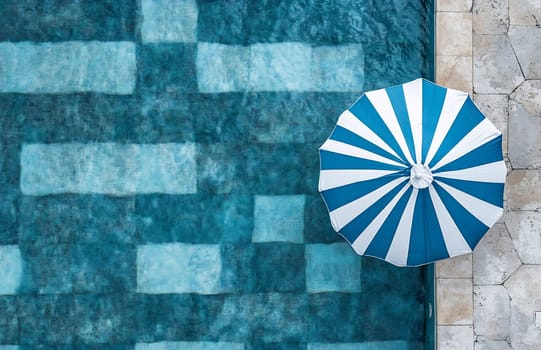 A striped umbrella shades a serene pool area with clear blue water and tiled flooring. Perfect for a peaceful retreat.