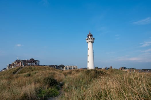 The approx. 28 m high white lighthouse J.C.J. van Speijk in Egmond aan Zee, North Holland, Netherlands with some of the town's houses with dune grass
