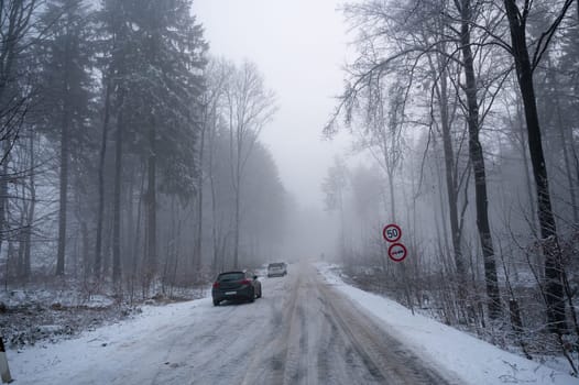 Snowy road in the countryside with lots of snow , fog and cars in a forest in Spessart, Bavaria, Germany
