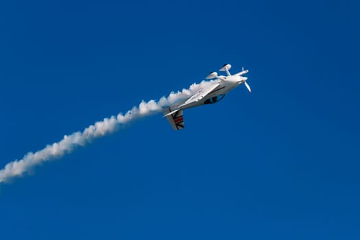 Stunt aerobatic plane performing stunts in blue sky with smoke trail. Concept of speed, difficulty, precision, risk, challenge