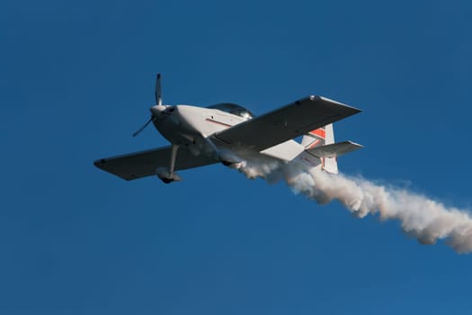 Stunt aerobatic plane performing stunts in blue sky with smoke trail. Concept of speed, difficulty, precision, risk, challenge
