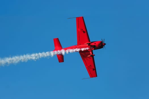 Red stunt aerobatic plane performing stunts in blue sky. Concept of speed, difficulty, precision, risk