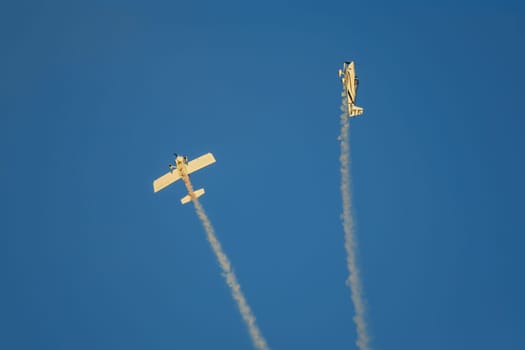Stunt aerobatic plane performing stunts in blue sky with smoke trail. Concept of teamwork, collaboration, coordination, trust, precision, difficulty, challenge, speed, synergy