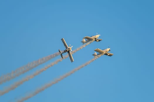 Three stunt aerobatic planes performing stunts in blue sky with smoke trail. Concept of teamwork, collaboration, coordination, trust, precision, difficulty, challenge, speed, synergy