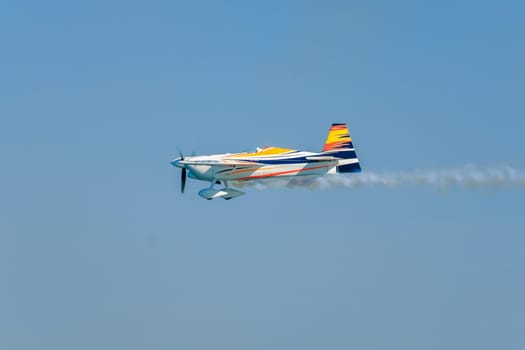 Stunt aerobatic plane performing stunts in blue sky with smoke trail. Concept of speed, difficulty, precision, risk, challenge