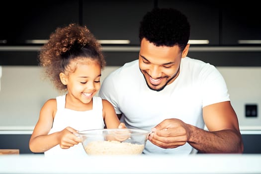 In a stylish kitchen, a father and his daughter enjoy a moment of joy as they prepare a meal together. The little girl, with curly hair, smiles brightly while mixing ingredients in a bowl.