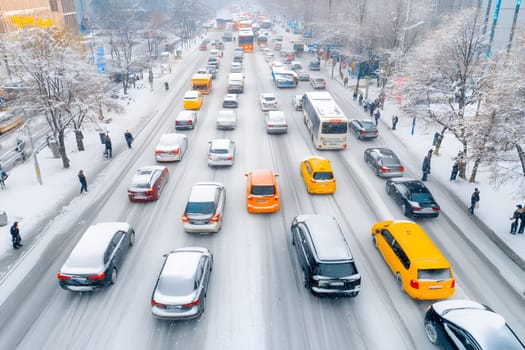 Blizzard has disrupted traffic in the city, as vehicles struggle to navigate through thick snow. Pedestrians are seen cautiously walking amid difficult winter conditions. High angle view