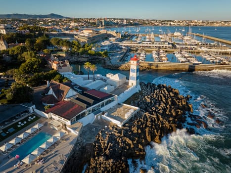 Aerial view of Santa Marta lighthouse and Cascais marina with moored yacht boats with Cascais cityscape, Portugal on sunset