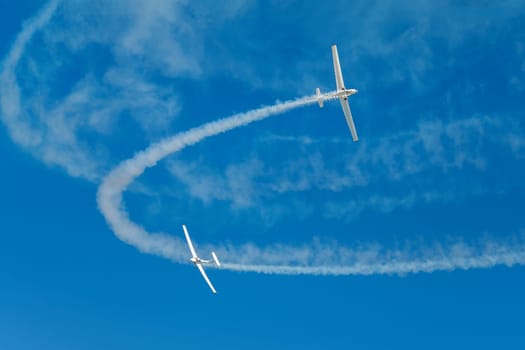 Stunt aerobatic plane performing stunts in blue sky with smoke trail. Concept of teamwork, collaboration, coordination, trust, precision, difficulty, challenge, speed, synergy
