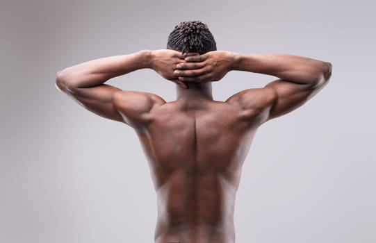 Shirtless sportsman posing with hands behind his head, highlighting strong back and arms while confidently gazing at the camera, exuding power and determination
