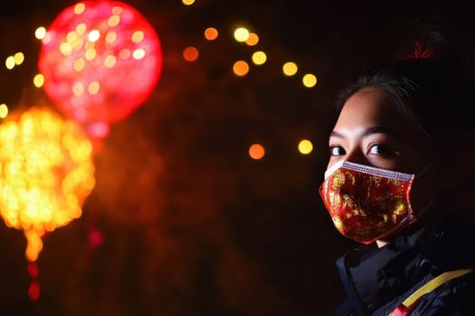 A person wearing a mask stands amidst colorful Christmas lights enjoying the festive atmosphere during nighttime celebrations.