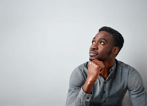 Portrait of young african american man relaxed with hand under chin looks pensive aside isolated on a grey wall background with copy space. Thoughtful male seeking for new ideas