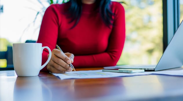 Businesswomen working about new startup on laptop to analysis finance of project. Woman holding a pen while working at office. Close up shot hands of woman use pen to analyze graphs and business data
