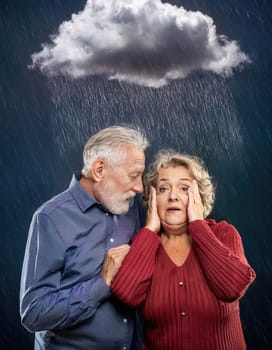 Senior couple standing together under rain, with a dark stormcloud above head. The old man hugs his wife as looks scared. Concept for Alzheimer's and dementia disease