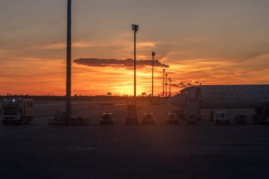 Suggestive view at sunset of the runway at Barcelona-El Prat airport. In the foreground a commercial aircraft of the low-cost airline Wizz Air with boarding ladder and service vehicles in position. The activity of the ramp agents suggests the preparation of an imminent flight.