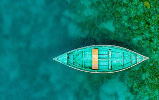 Aerial view of turquoise wooden boat on vibrant teal water surface.