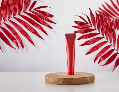 Red plastic tube for cosmetics on wooden stand, white background with red leaves