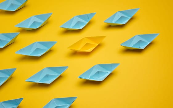 Group of paper boats rushing forward on yellow background, achieving goals