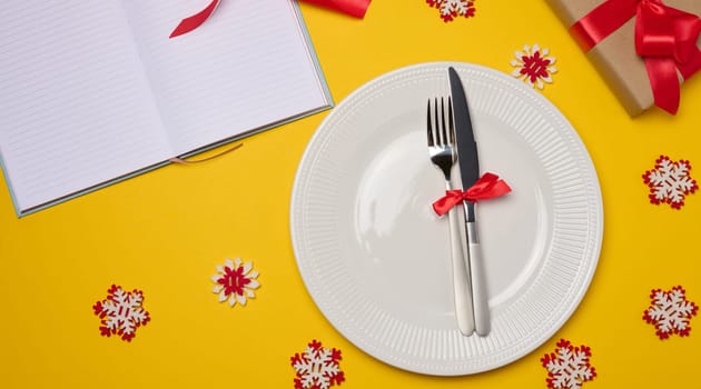 Empty white round plate, fork and knife on yellow background, top view