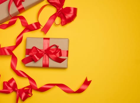 Two boxes tied with red ribbon on yellow background, festive background.