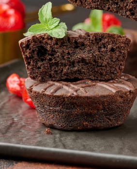A stack of rich chocolate brownies topped with a glossy cherry and fresh mint leaf, standing on a dark background